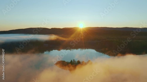 Flying through the clouds above lake surrounded by forest and mountain range