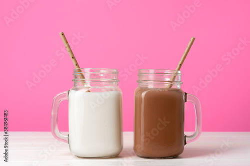 Glass jars with flavoured milkshakes against pink background