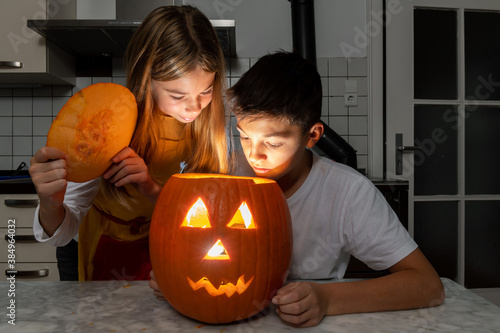 Junge und Mädchen bestaunen Ihren selbst geschnitzten Kürbis der schaurig schön in der Halloween Zeit leuchtet. photo