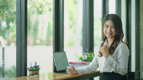 Portrait of a young attractive Asian woman relaxing while sitting at her office desk, smiling and looking at the camera.