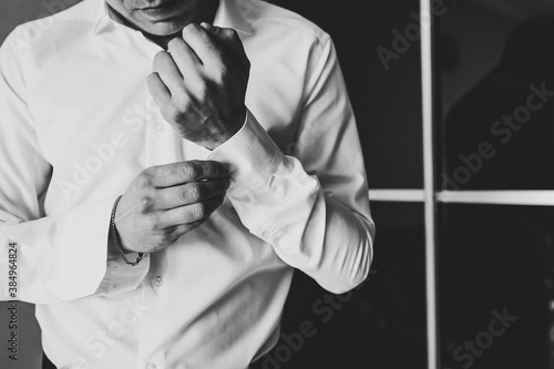 Hand's groom wears a metallic silver cufflinks stud. Wedding morning. Black and white photo.