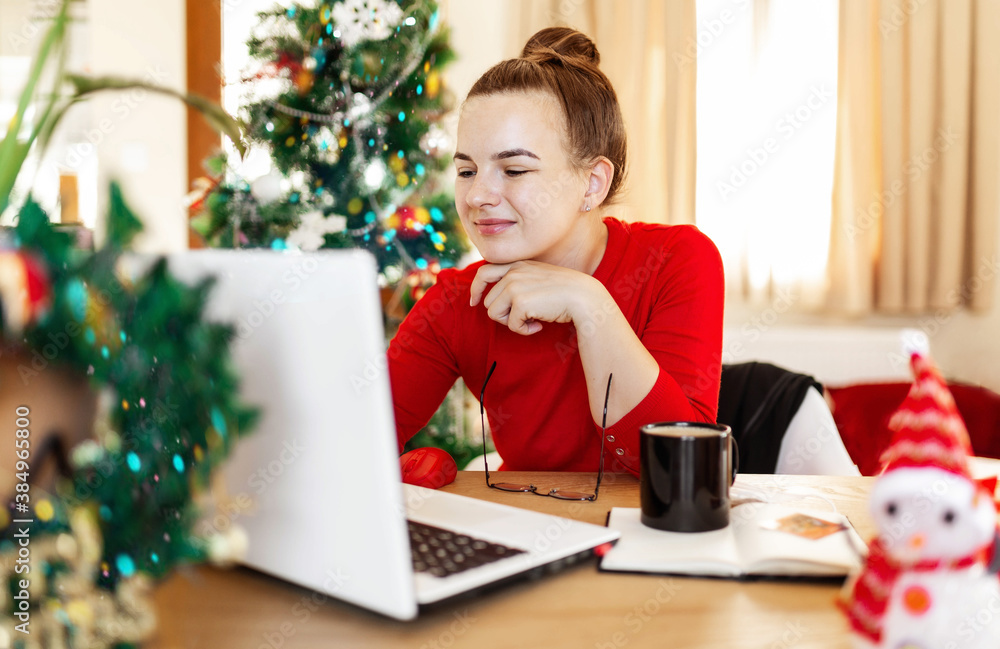 Young attractive woman in red sweater working at home during christmas holidays, white laptop, New Year tree Young attractive woman in red sweater working at home during christmas holidays, white laptop, New Year tree
