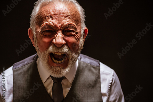 Portrait of furious senior man who is screaming. Black background. photo