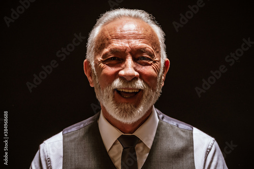 Portrait of cheerful senior man on black background.