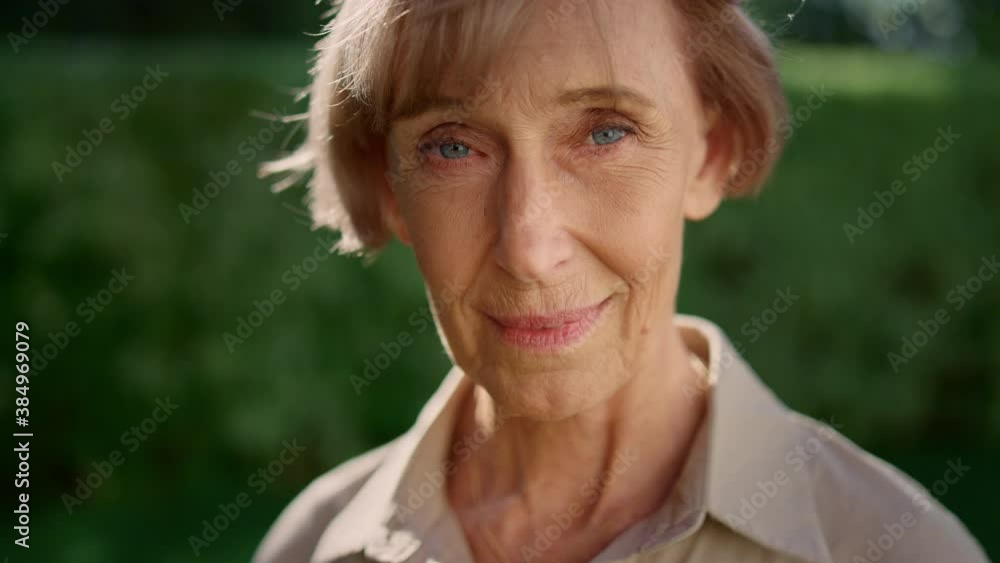 Smiling senior woman posing at camera in summer garden. Senior lady looking down