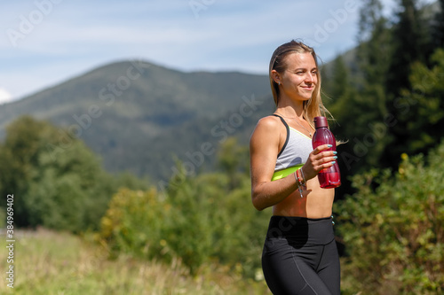 Fit young woman stretching legs and looking at camera. Caucasian female exercising at the park in morning. drinking water