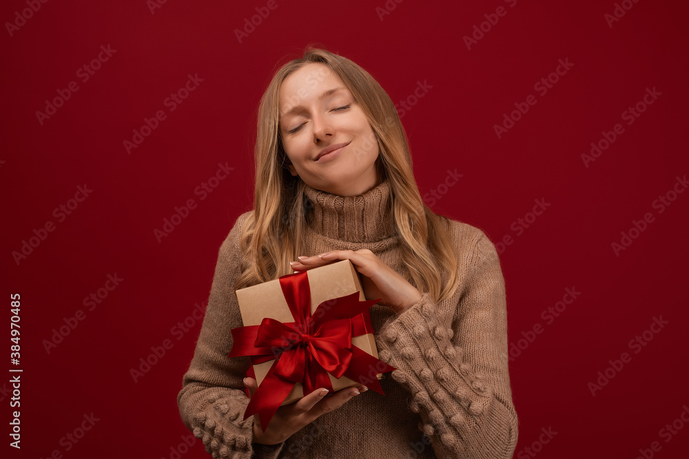 Charming blonde woman holding gift with red ribbon. Studio shot red background. New Year Birthday Holiday concept Charming blonde woman holding gift with red ribbon. Studio shot red background. New Year Birthday Holiday concept