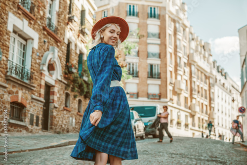 Happy, smiling woman wearing stylish autumn blue checkered dress, orange hat, wide white belt, walking in street of Paris. Copy, empty space for text photo