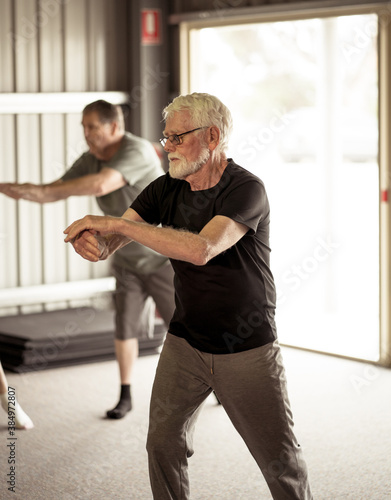 Group of elderly senior people practicing Tai chi class in age care gym facilities.