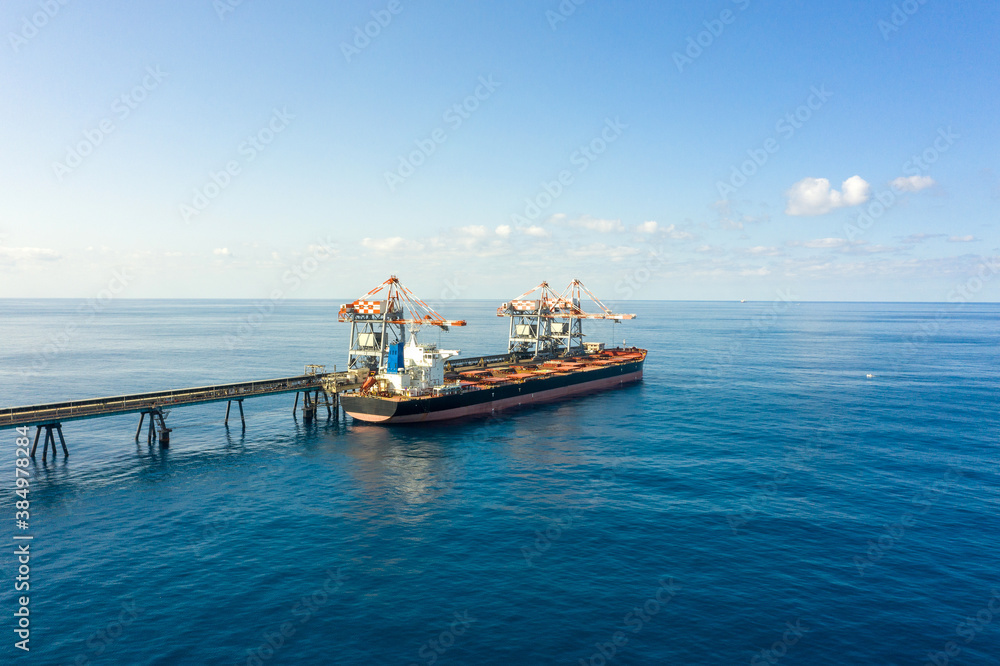 Obraz premium Coal carrier Cargo Ship docked at a commercial pier during unloading operation, Aerial view. 