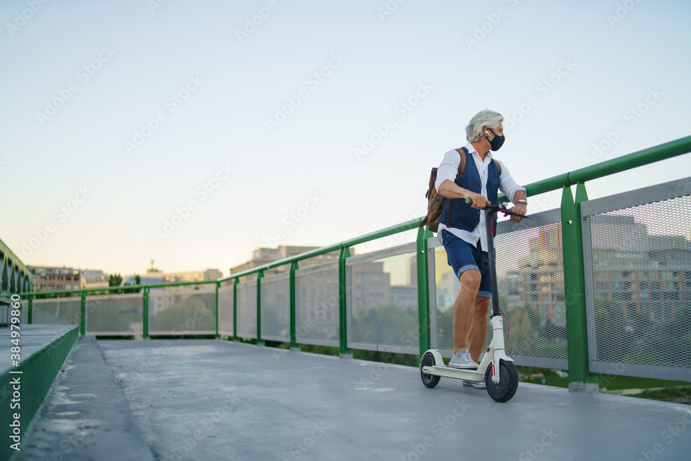Mature man commuter with face mask and electric scooter outdoors in city, coronavirus concept. Mature man commuter with face mask and electric scooter outdoors in city, coronavirus concept.