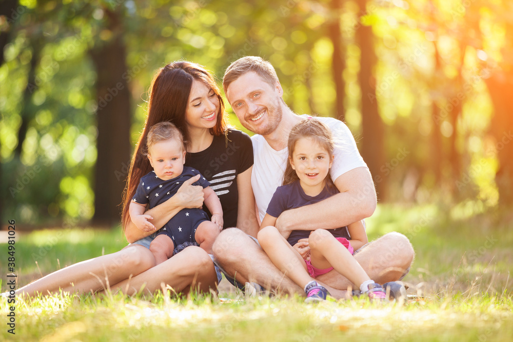 Happy mother, father, son and daughter in the park. Beauty nature scene with family outdoor lifestyle. Happy family resting together sitting on the grass, having fun outdoor. Happiness and harmony