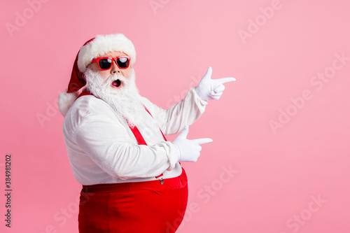 Profile side photo of astonished santa claus point index finger copyspace x-mas ads wear sunglass headwear suspenders headwear isolated over pastel color background photo