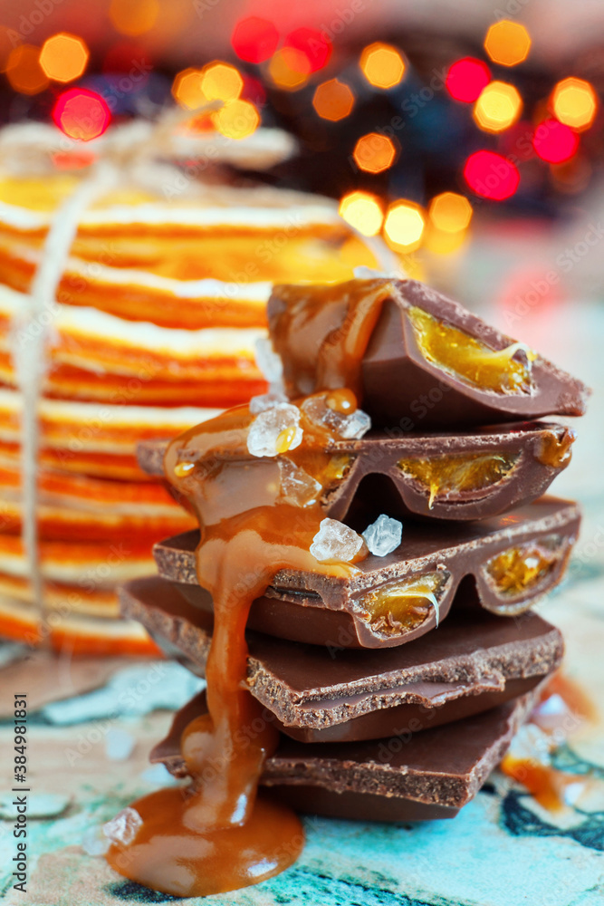 Macro chocolate pieces with caramel and sea salt against holiday background and dried oranges