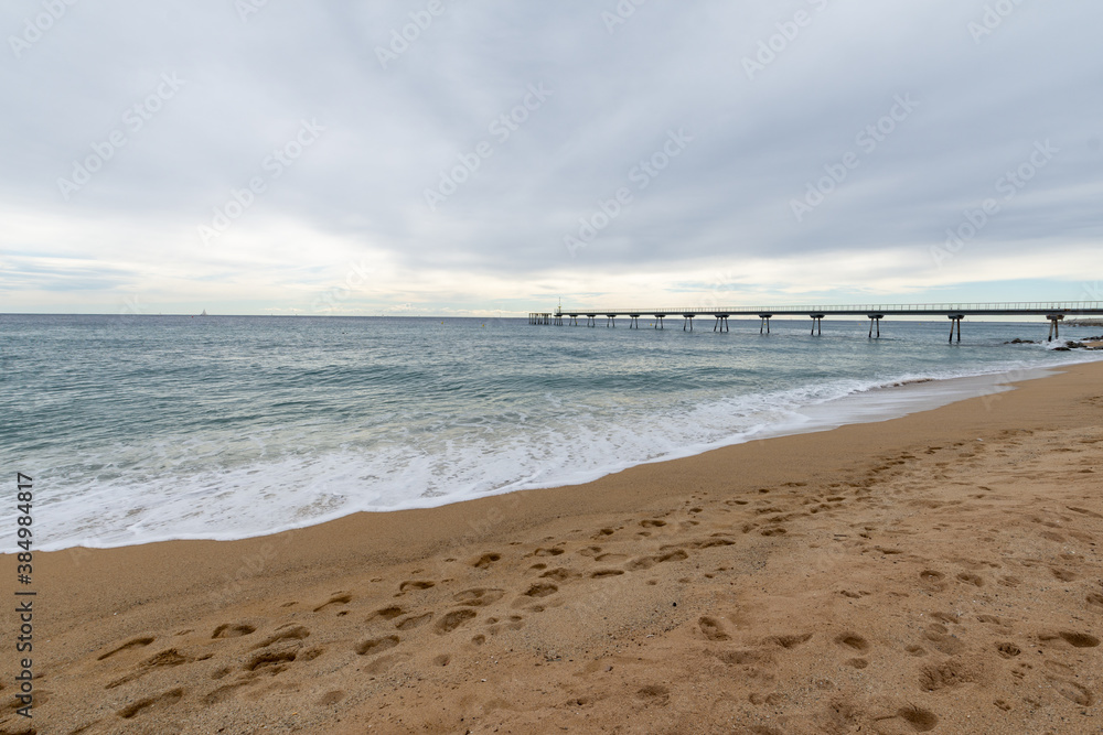 View of footsteps on the beach, with a walkway in the background, a cloudy day, in Badalona, Spain, horizontal