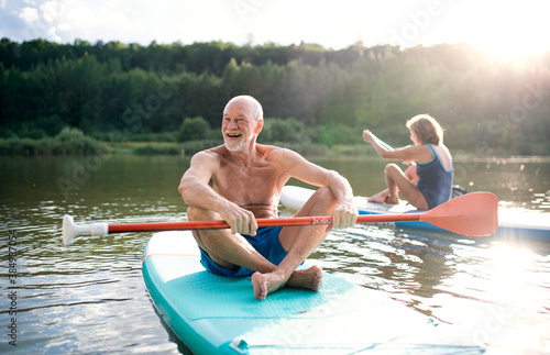 Senior couple paddleboarding on lake in summer. © Halfpoint