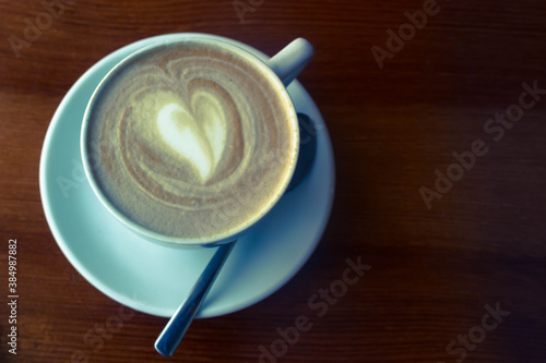 A Cup of coffee, a heart made of coffee foam. Coffee in a white Cup with a spoon in a cafe is on the table.