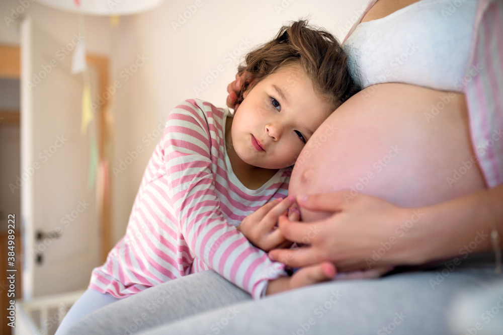 Small girl hugging belly of unrecognizable pregnant mother indoors at home. Small girl hugging belly of unrecognizable pregnant mother indoors at home.