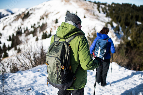 Rear view of senior couple hikers in snow-covered winter nature, walking.