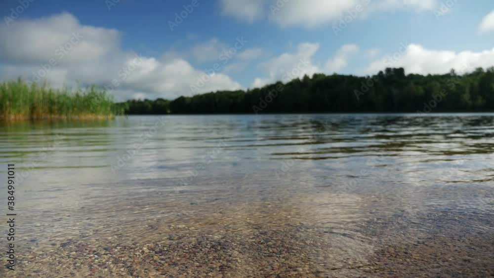 The clear water of the lake washes the shore of small pebbles, low angle static shot, slow motion. The clear water of the lake washes the shore of small pebbles, low angle static shot, slow motion.