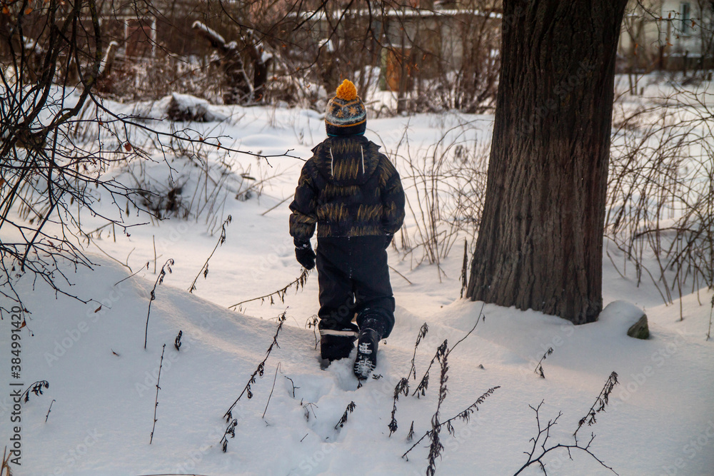 Baby toddler boy walking in the snow in winter far away in the Park.