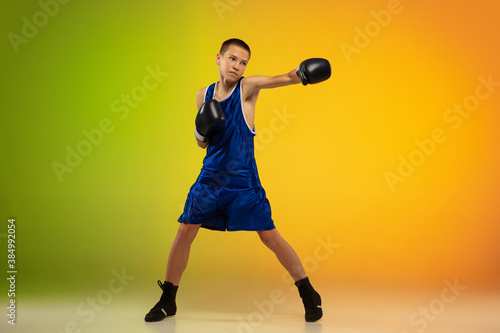 Fighter. Teenage professional boxer training in action, motion isolated on gradient background in neon light. Kicking, boxing. Concept of sport, movement, energy and dynamic, healthy lifestyle. © master1305