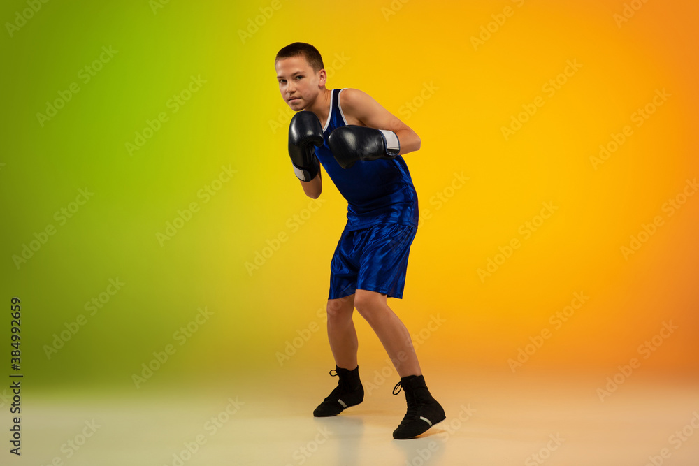 Emotional. Teenage professional boxer training in action, motion isolated on gradient background in neon light. Kicking, boxing. Concept of sport, movement, energy and dynamic, healthy lifestyle.