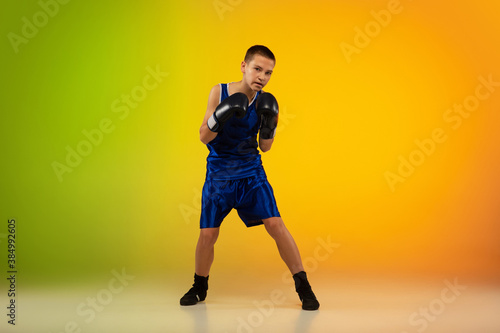 Emotional. Teenage professional boxer training in action  motion isolated on gradient background in neon light. Kicking  boxing. Concept of sport  movement  energy and dynamic  healthy lifestyle.