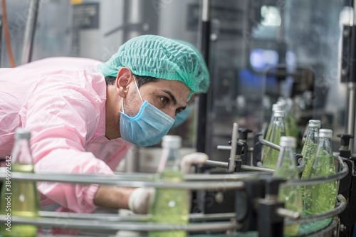 Bild auf Leinwand Male workers in factory uniforms wear masks, hair hoods, and a fruit juice quality inspector in a healthy drinking water production line in a nectarine factory