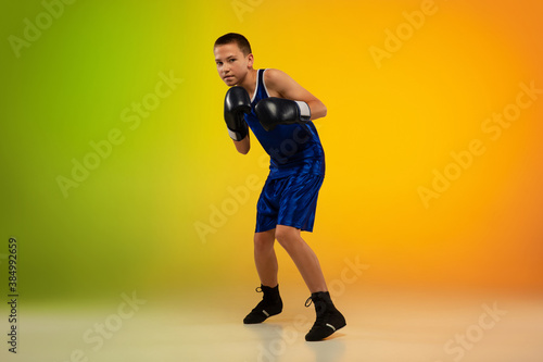Emotional. Teenage professional boxer training in action, motion isolated on gradient background in neon light. Kicking, boxing. Concept of sport, movement, energy and dynamic, healthy lifestyle. © master1305