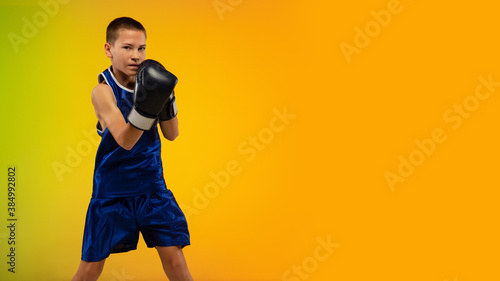 Winner. Teenage professional boxer training in action, motion isolated on gradient background in neon light. Kicking, boxing. Concept of sport, movement, energy and dynamic, healthy lifestyle. Flyer