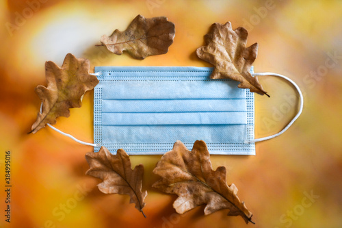 Photography A medical protective mask and yellow dry oak leaves lie on a bright autumn background