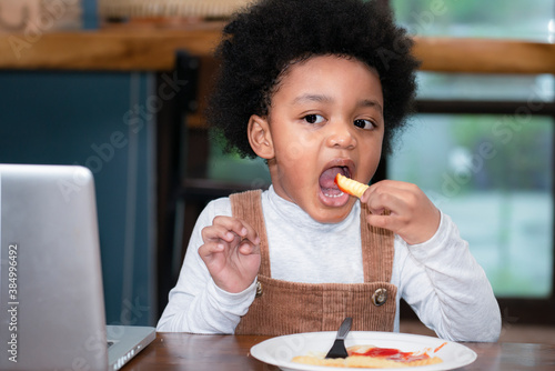 Portrait of small little cute  black boy eating french fries potato at the table in the restaurant. African American boy enjoy eating french fries. Enjoy eating.