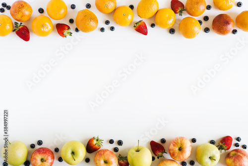 Food frame background. Fruits and berries on white table, top view, space for text. Oranges, apples, strawberry, blueberry layout