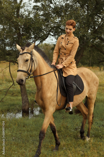 Young cow girl walking horse in green field. People and animal portrait. Horseback riding view. Active weekend. Beautiful young woman walking with brown horse on green field 