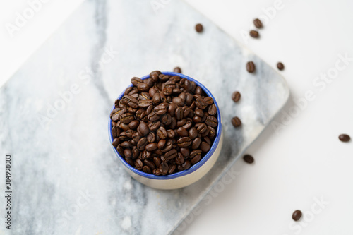 Coffee beans in a bowl on marble, overhead view