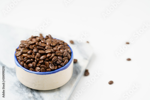 Coffee beans in ceramic bowl with blue rim on white table and marble board