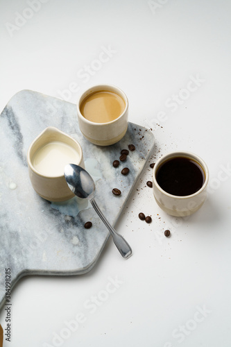 Coffee and milk in ceramic cups with beans, marble