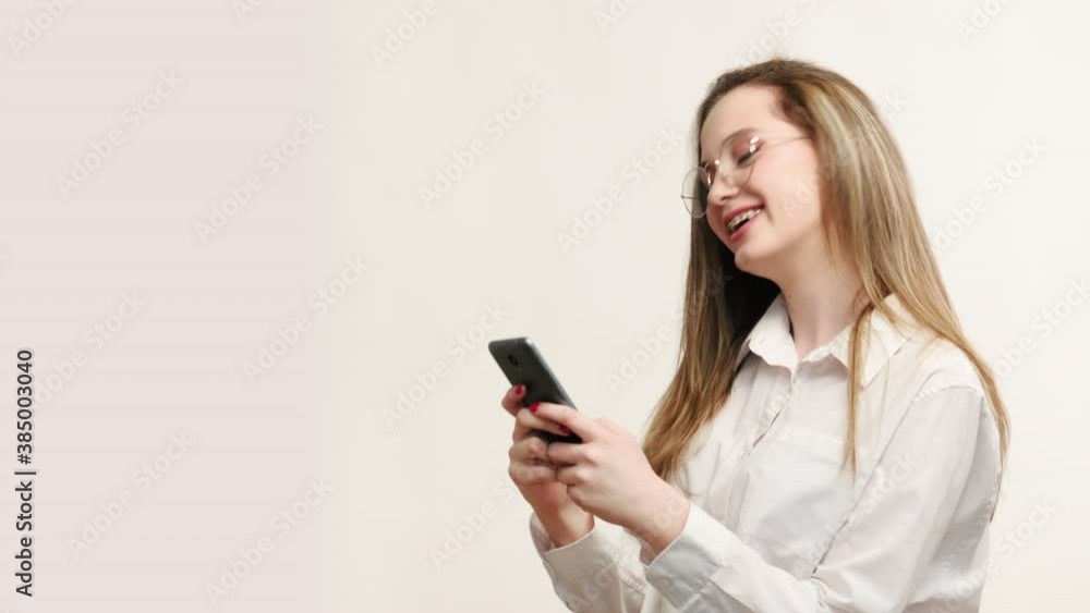 Friendly chat. Online communication. Amused business woman in glasses reading texting message on phone laughing smiling isolated on light copy space background. Mobile technology. New normal. Friendly chat. Online communication. Amused business woman in glasses reading texting message on phone laughing smiling isolated on light copy space background. Mobile technology. New normal.