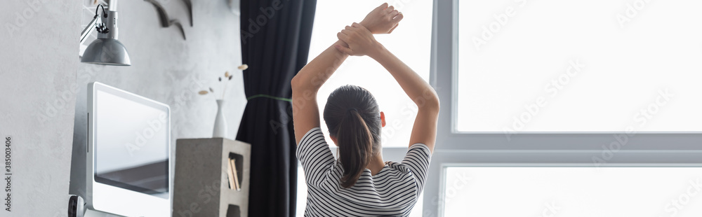 Fototapeta premium Panoramic shot of woman looking at window while sitting near computer at home