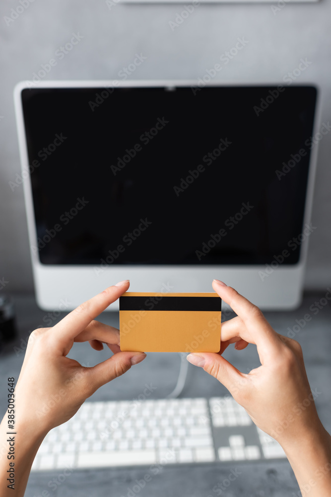 Cropped view of woman holding credit card near computer at home
