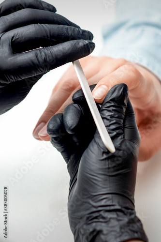 Closeup shot of young woman getting manicure by manicure master with nail file in nail salon