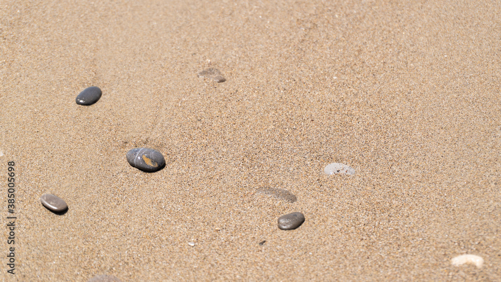 Small gray wet stones on golden beach sand. Copy space. Wet sand and small stones on the seashore Small gray wet stones on golden beach sand. Copy space. Wet sand and small stones on the seashore