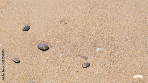 Small gray wet stones on golden beach sand. Copy space. Wet sand and small stones on the seashore