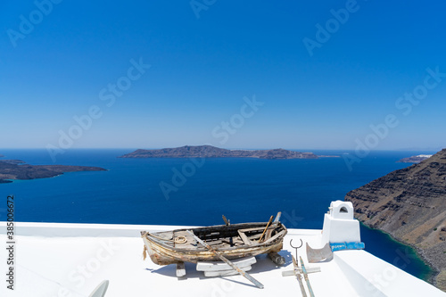 Old boat for decoration on a white roof of a house of Santorini island, Greece. Blue Mediterranean sea and Santorini caldera in the background