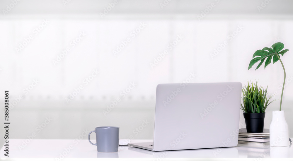 Fototapeta premium Mockup laptop computer with mug, houseplant and vase on white top table in white room