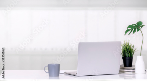 Mockup laptop computer with mug  houseplant and vase on white top table in white room