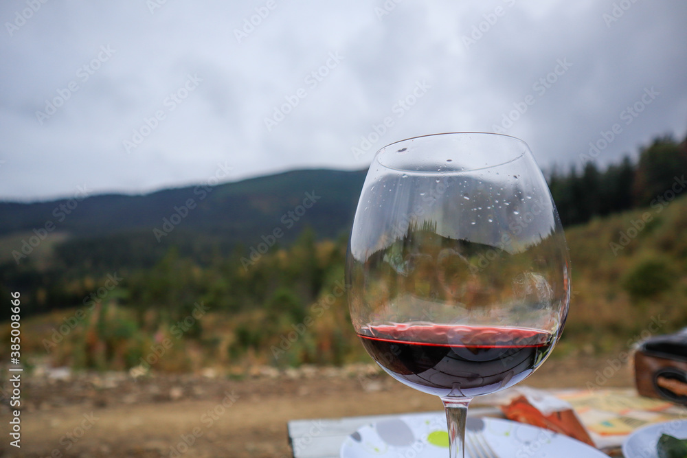 Photo of wine pouring out of a glass on a background of mountains. Female hand. Ukrainian Carpathian Mountains