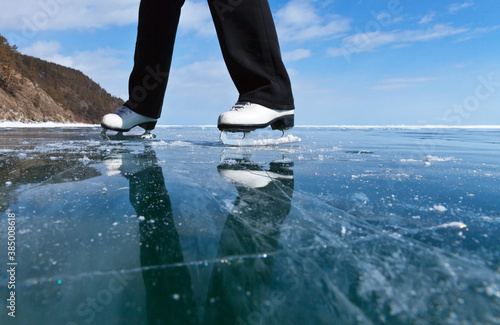 Fun ice skating on frozen lake on sunny winter day. View of beautiful transparent blue ice of frozen Baikal Lake. A girl in white figure skates travels on the ice. Winter outdoor activities concept