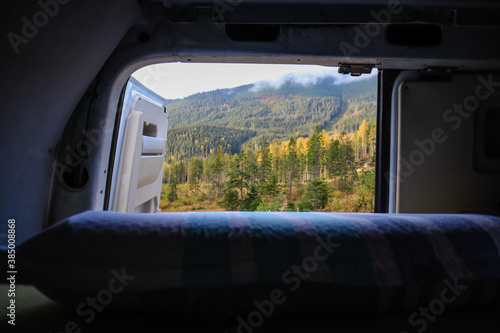 Traveling on a camper in Ukraine. View from the camper in the morning on the mountains in the clouds. Bed and legs. Person in camping van open door.